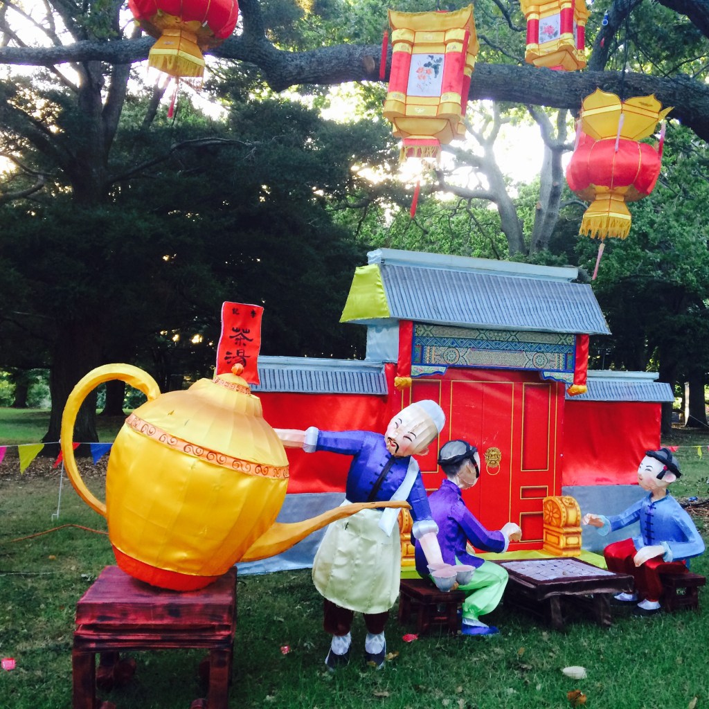 Colorful outdoor display with teapot, cups, and lanterns in a garden.